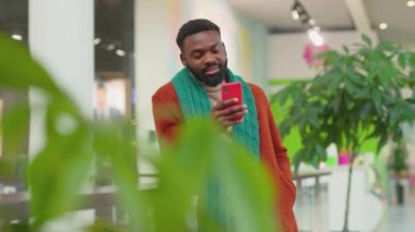 Yakışıklı Afrikalı Amerikalı genç adam Noel zamanı alışveriş merkezinde telefon kulübesi kullanıyor mutlu bir gülümseme alışverişi yapıyor interneti kapatıyor mobil teknolojiyi yavaş çekimde kapatıyor