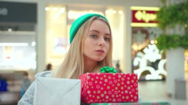 Genç, güzel bir kadın Noel hediyeleriyle birlikte şapka askısı takıyor alışveriş merkezindeki kutuları dikkatlice tutuyor. Etrafına bak. Yeni yıl tatili için ciddi bir portre al.