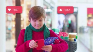 Çocuk elinde Noel hediyesi kutularıyla alışveriş merkezinde duruyor. Çocuk telefonu kullanıyor. Çocuk ailesi sosyal medya simgeleri kullanıyor.