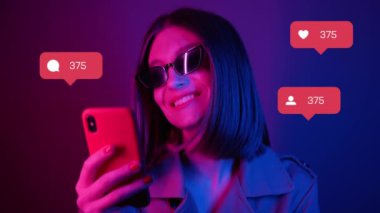 Renkli ışık kullanan genç bir kadın yorum yapan takipçi sayacı gibi sosyal medya simgeleri yazarak blog yazarı, yetişkin iletişim interneti blogu, yavaş çekim moda portresi