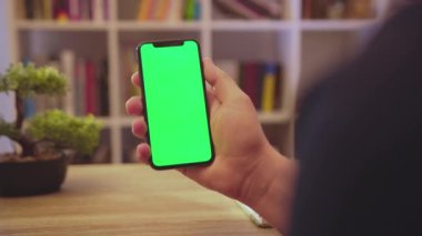 NEW YORK - 19 Mayıs 2019: Masa görevlileri telefonu dikey yeşil ekran kullanımıyla tutun dokunma dijital akıllı telefon ev iletişim teknolojisi internet krom sosyal medya arka plana yavaşça tıklayın