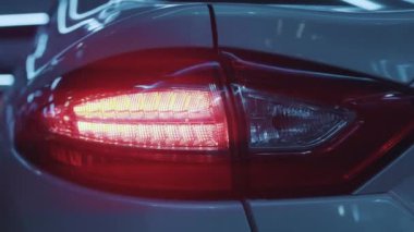 Araba detayı. Modern beyaz araba stop lambaları yakın plan kırmızı parlıyor. Açık otoparkta karanlıkta yanıp sönen lüks spor arabanın arka farları..