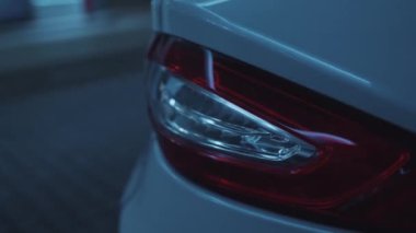 Yeraltı otoparkına park edilmiş modern lüks beyaz arabanın arka görüntüsü. Kırmızı kablo, kameraya yanıp sönen arka farları yaktı. Araba ayrıntıları konsepti.