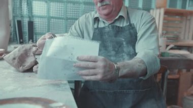 Lviv, Ukrayna - 7 Ocak 2020: Çömlek atölyesinde çalışırken gururla çizimlerine bakan neşeli çömlekçi büyükbaba portresi. Sanatçı.