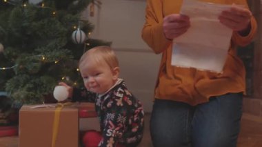 Lviv, Ukrayna - 7 Ocak 2020: Noel oyuncaklarıyla oynayan süveterli tatlı bir bebek, büyükannesiyle yerde oturuyor. Aile ve çocuklar. Birleşme konsepti.