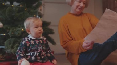 Lviv, Ukrayna - 7 Ocak 2020: Güzel, mutlu bir büyükanne, küçük torunuyla oynarken, evde Noel ağacının yanında birlikte duran tatlı bir bebekle konuşan bir resim gösteriyor..