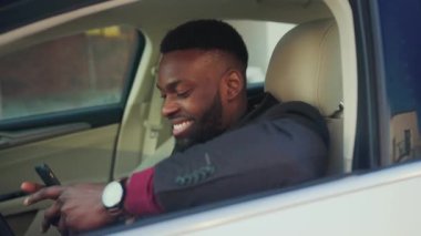 Çevrimiçi Aktarmalı Uygulama Simgesi. Smartphone 'daki finansal işlemler. Parayı Artırma ile ilgili bir mesaj al. Mutlu Afro-Amerikalı genç iş adamı. Telefonunu arabada kullan. Gülümse. Arkasında oturuyor.