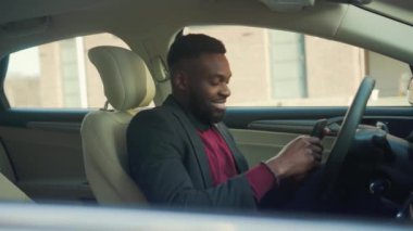 Çevrimiçi Aktarmalı Uygulama Simgesi. Smartphone 'daki finansal işlemler. Parayı Artırma ile ilgili bir mesaj al. Mutlu Afro-Amerikalı genç iş adamı. Telefonunu arabada kullan. Gülümse. Arkasında oturuyor.