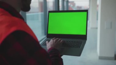 El mühendisi, bina işçilerinin içinde yeşil ekranlı dizüstü bilgisayar kullanıyor. İşgal teknolojisi. Profesyonel erkek güvenlik aygıtı yavaş çekim bilgisayarı.