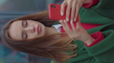 Dikey ekran videoda genç bir kadın sokak portresi üzerinde telefon standı kullanıyor. Akıllı telefon, beyaz kadın iletişim aracı yaşam tarzı teknolojisi yavaş çekim.