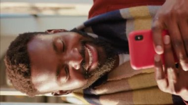 Portre gülümseyen Afrikalı Amerikalı genç adam tramvay trafiğinde akıllı telefon kullanıyor. Güneşli bir günde daktilo yazıyor. Yakışıklı yolcular internetteki dikey video ekranı yavaş çekim.