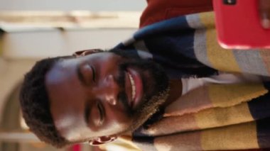 Yüzünüzü kapatın gülümseyen Afrikalı Amerikalı genç adam tramvayda otururken akıllı telefon kullanıyor güneşli bir günde yakışıklı yolcular internetteki dikey video ekranı yavaş çekim tarzında daktilo ediyor.