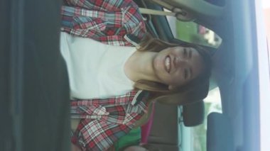 Mutlu anne ve heyecanlı çocukları gülümsüyor. Şehirli bir ailenin arabasında oturuyorlar. Yaz aylarında dikey çekimde arabayla seyahat ediyorlar.