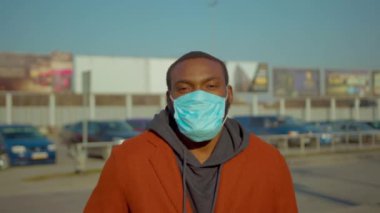 COVID-19 koronavirüs enfeksiyonundan korunmak için koruyucu maske takan Afrikalı Amerikalı bir adam havaalanı salgını salgını olan erkek turist hava hastalığının yakınındaki kameraya bakın.