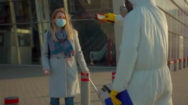 Koruyucu giysili bir sağlık çalışanı, yolcuyu tarayıp kadının üzerine antiseptik serperek Coronavirus kontrol noktaları Coronavirus kontrol noktaları salgınını maskelemeye çalışıyor.