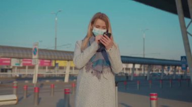 Koruyucu Yüz Maskesi takan genç bir kadın havaalanı yakınında telefon kulübesi kullanıyor COVID-19 Coronavirus enfeksiyonu salgını virüsü erkek turist salgını hava sağlığı hastalığı yavaş çekim