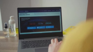 NEW YORK - 28 Mart 2020: Masadaki dizüstü bilgisayarda evde oturup haber içeriği koronavirüs salgınını okuyan genç adam. Yakın plan. Karantinaya alın. Dünya çapında hastalıklar.