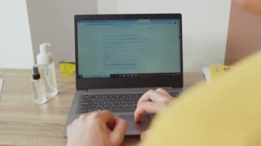 NEW YORK - 28 Mart 2020: Evde Coronavirus hakkında makale okuyan genç bir adamın yan görüntüsü. Dünya çapında dizüstü bilgisayarla çalışan salgınlar hakkında yakın plan kişilere bilgi veriliyor..