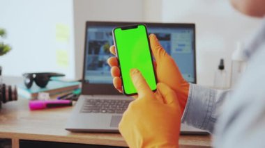 NEW YORK - 28 Mart 2020: Evde çalışırken dikey krom akıllı telefon kullanan genç yetişkin. Yakın plan adam mobil uygulamalara bakıyor ve ameliyat eldiveni takıyor. Karantina.