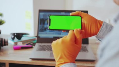 NEW YORK - 28 Mart 2020: Evden çalışan akıllı telefon uygulaması ile çalışan genç bir adamın el bilgisayarı. Yakın plan. Frelancer. Eldivenler el koruması. Sağlık hizmetleri.