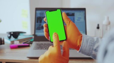 NEW YORK - 28 Mart 2020: Akıllı telefon dikey yeşil ekran maket uygulaması kullanan adama yakın çekim. Evde dizüstü bilgisayarla çalışan genç yetişkinlerin cep telefonu haberlerinin el kamerası görüntüleri..