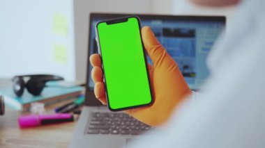 NEW YORK - 28 Mart 2020: Akıllı telefon uygulaması sosyal medya dikey yeşil ekranını tıkırdatan tıbbi eldiven takan genç bir adamın yakın çekimi. Uzak bir iş. Karantina.