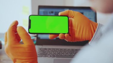NEW YORK - 28 Mart 2020: Cerrahi eldivenli yakın plan doktor elinde yatay akıllı telefon, koronavirüs haber istatistikleri evde oturuyor. Uzak bir iş. Karantinaya alın. Sağlık hizmetleri.