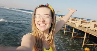 Gözlüklü çekici genç bir kadın el sallıyor gülümsüyor konuşuyor Mısır 'da denizde mutlu hissediyor aşk insanı çift doğada güneş gökyüzü Afrika selfie seyahati tatil aktivitesi arıyor