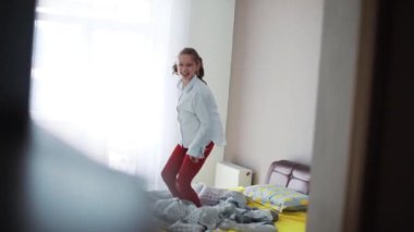 Gülümseyen, uzun saçlı genç ve çekici bir kız lüks bir dairede yatakta eğleniyor mutlu çocuk partisi kızı ev dansı teknolojisi aktif çocukluk yavaş çekim portresi.