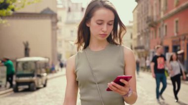 Parlak gün ışığında genç bir kadının portresi şehir merkezinde telefon yürüyüşü yapıyor saçlarını okşuyor ve teknolojinin dışındaki ciddi internet sektörüne bakıyor.