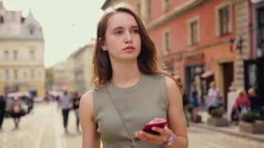 Parlak güneş ışığı altında ciddi bir genç kadın şehir merkezinde telefon yürüyüşü yapıyor saçlarını okşuyor teknolojinin dışındaki güzel yaz internet işine bakıyor.