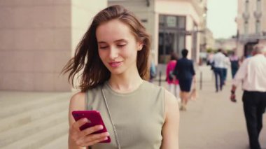 Parlak güneş ışığı altında gülümseyen genç bir kadın telefon kullanıyor. Yazın şehir merkezinde internet işinde teknolojinin dışında duruyor.