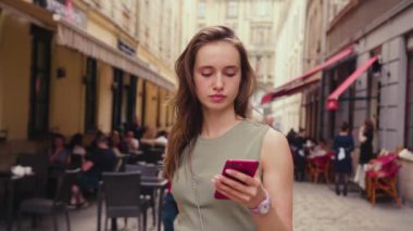 Parlak güneş ışığı altında ciddi genç bir kadın şehir merkezinde yürürken kırmızı telefon kullanıyor. Yazın internet işi teknolojinin dışında.