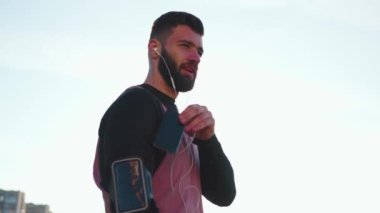 Yakından bir adam sportmen, spor kıyafetleri içinde telefonla konuşur dışarıda koşar günbatımını dinler spor fitness adamı teknoloji eğitimi güneş ışığı portresi yapar