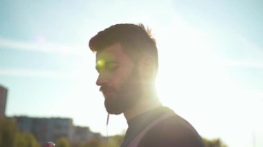 Portre yakışıklı genç sporcu kulaklık takıyor. Spor kıyafetleri giyiyor. Dışarıda koşuyor.