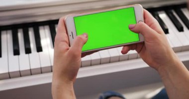 Tokio, Japonya - 7 Nisan 2018. Yatay yeşil ekranlı akıllı telefon kullanan genç bir kadın arka planda piyano kromakey beyaz cihaz zengin palmiyeler tatil köyü modern yaşam tarzı