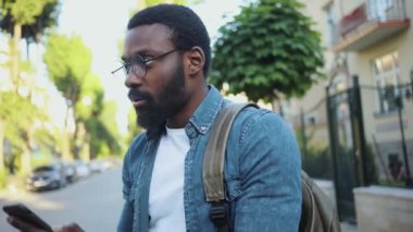 Kapatın gözlüklü genç Afrikalı Amerikalı adam gülümseyin sokak güneşinde mutlu olun internet teknolojisi mesajı yakışıklı akıllı telefon mesajları seyahat portresi dışında.