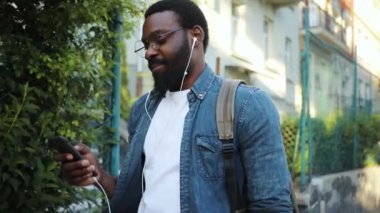 Gözlüklü genç Afrikalı Amerikalı adam, dinle. Telefon kullan. Sokakta yürü, gülümse.