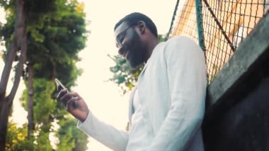 Sokak tebessümü üzerinde telefon kullanan Afro-Amerikan genç çekici adam mutlu günbatımı günbatımı cep telefonu bilgisayar moda interneti teknoloji işadamları siyah şehir gezgini