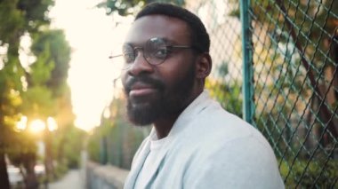 Kapatın gözlüklü Afro-Amerikalı genç adam gülümseyin mutlu görünün doğa teknolojisi güneş günlük siyah yakışıklı dış sakal neşeli şehir ağır çekim