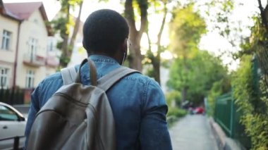 Arkadaki genç turist Afrikalı Amerikalı adam şehirde geziyor. Kulaklıkla müzik dinliyor. Gün batımında günbatımında güneş ışığı tatili seyahati.