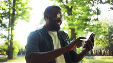 Mutlu afro-amerikan genç çekici adam sokakta yürürken gülümsüyor güneş ışığı günbatımı cep telefonu bilgisayar moda interneti teknoloji işadamları siyah şehir ağır çekim