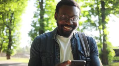 Gülümseyen Afro-Amerikan genç çekici adam, gün batımı caddesinde telefon yürüyüşü yapıyor. Cep telefonu, bilgisayar, internet, teknoloji işadamları, siyahi genç şehir gezici portresini kapatıyor.