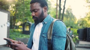 Ciddi Afro-Amerikan genç ve çekici bir adamın telefon kullanması günbatımında caddede durması cep telefonu bilgisayar moda interneti teknoloji işadamları siyah şehir gezginleri ile yüz yüze.
