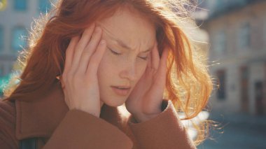 Mutsuz, mutsuz, genç bir kadın. Şakaklarına masaj yapıyor. Sokakta şiddetli baş ağrısı çekiyor. Sağlık sorunları. Hastalık, grip gibi. Coronavirus belirtileri.