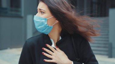 Yüzü maskeli genç bir iş kadını akıllı telefondan Coronavirus hakkında haber akışını kontrol ediyor. Ofisten eve dönerken nefes almakta güçlük çekiyor..