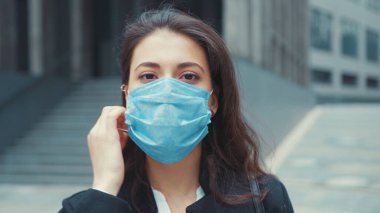 Beyaz, güzel, genç, esmer kadın, yönetici ofis yöneticisi. Solunum maskesini çıkarıyor. Dışarıdaki kamerada mutlu görünüyor. Karantina sona erdi. Salgın.