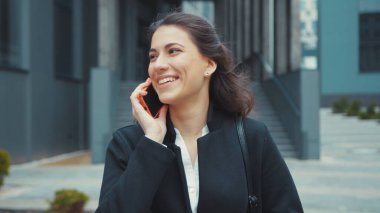 Binanın dışında akıllı telefon uygulaması kullanarak yürüyen genç bir bayanın sosyal medyada neşeli ve rahat bir şekilde mesajlaşması..