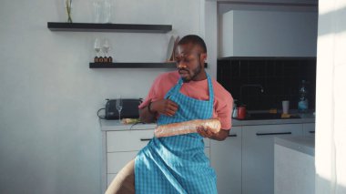 Komik Afro-Amerikalı adam apron dansı yapıyor ve mutfakta ekmek somunuyla eğleniyor. Çılgın aşçı aşçılığı. Eğlence. Daire. Kapalı.