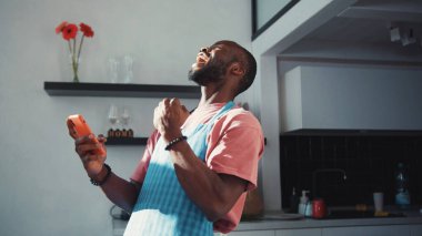Afro-Amerikalı çekici bir adam yemek pişirirken internette geziniyor. Akıllı telefondan mesaj aldığında gülümseyen neşeli siyahi adam. İç mekanlar. Ev hayatı. Teknoloji.